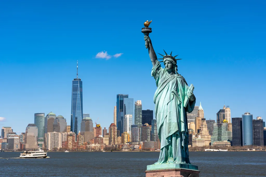 The Statue of Liberty in the foreground with the Lower Manhattan skyline, including One World Trade Center, in the background.