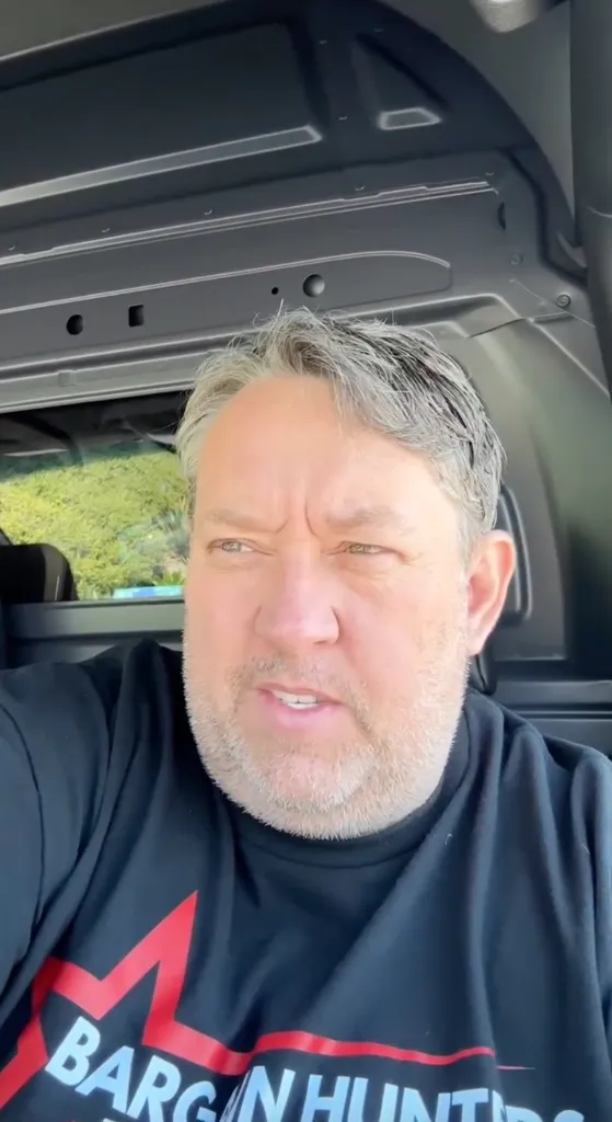 A man with graying hair and a beard, wearing a black t-shirt with 