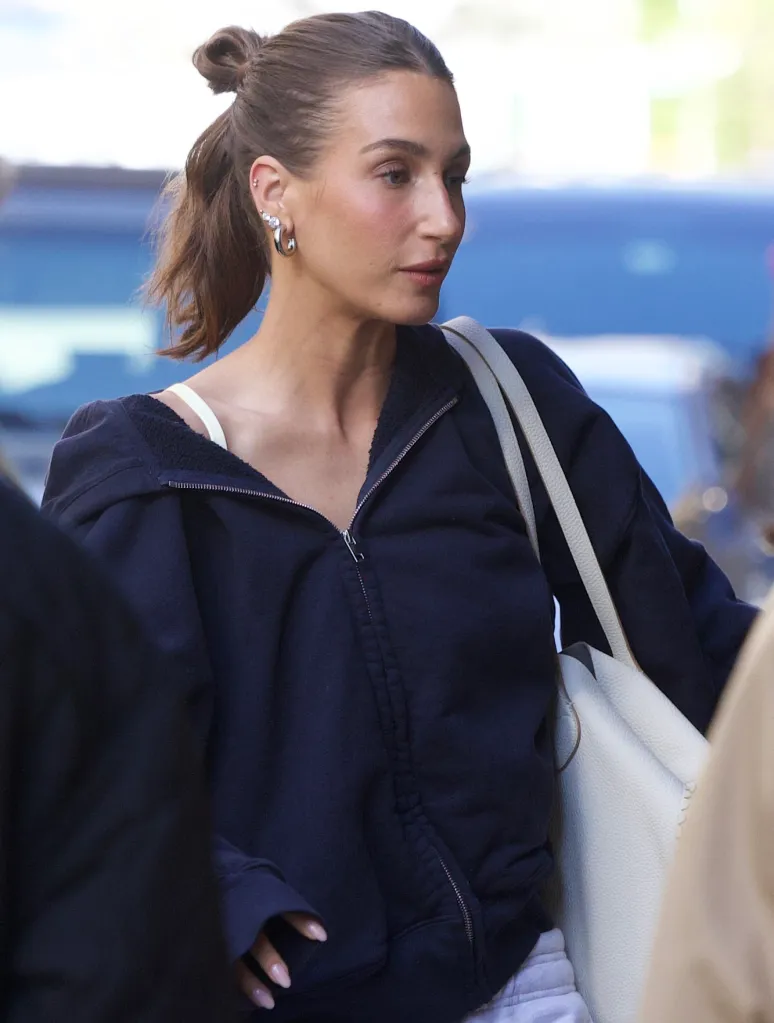 A woman in a navy blue zip-up hoodie and white bra with a white bag on her shoulder.