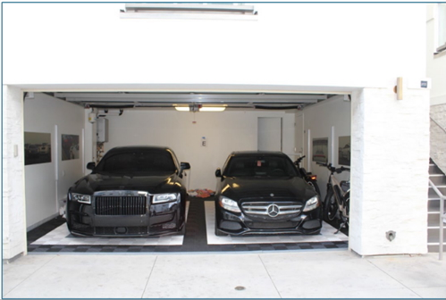 A black Rolls-Royce Ghost and a black Mercedes-Benz parked in a garage.