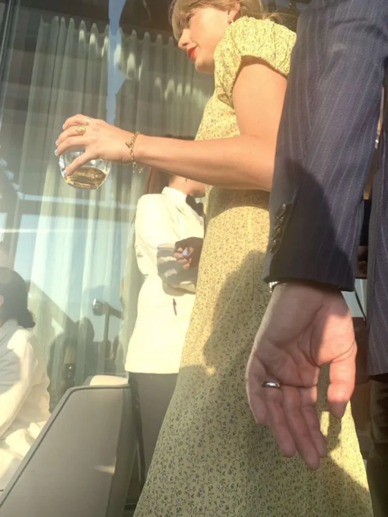 Taylor Swift in a yellow floral dress holding a drink, next to Matty Healy and others at Cipriani.