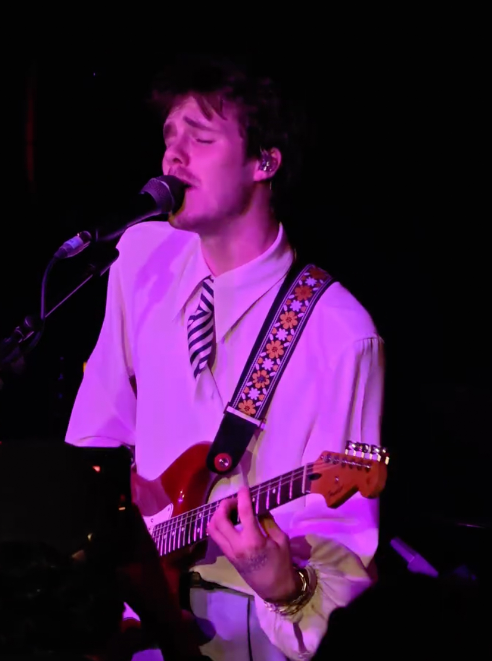 Cruz Beckham performing with a guitar on stage, singing into a microphone.