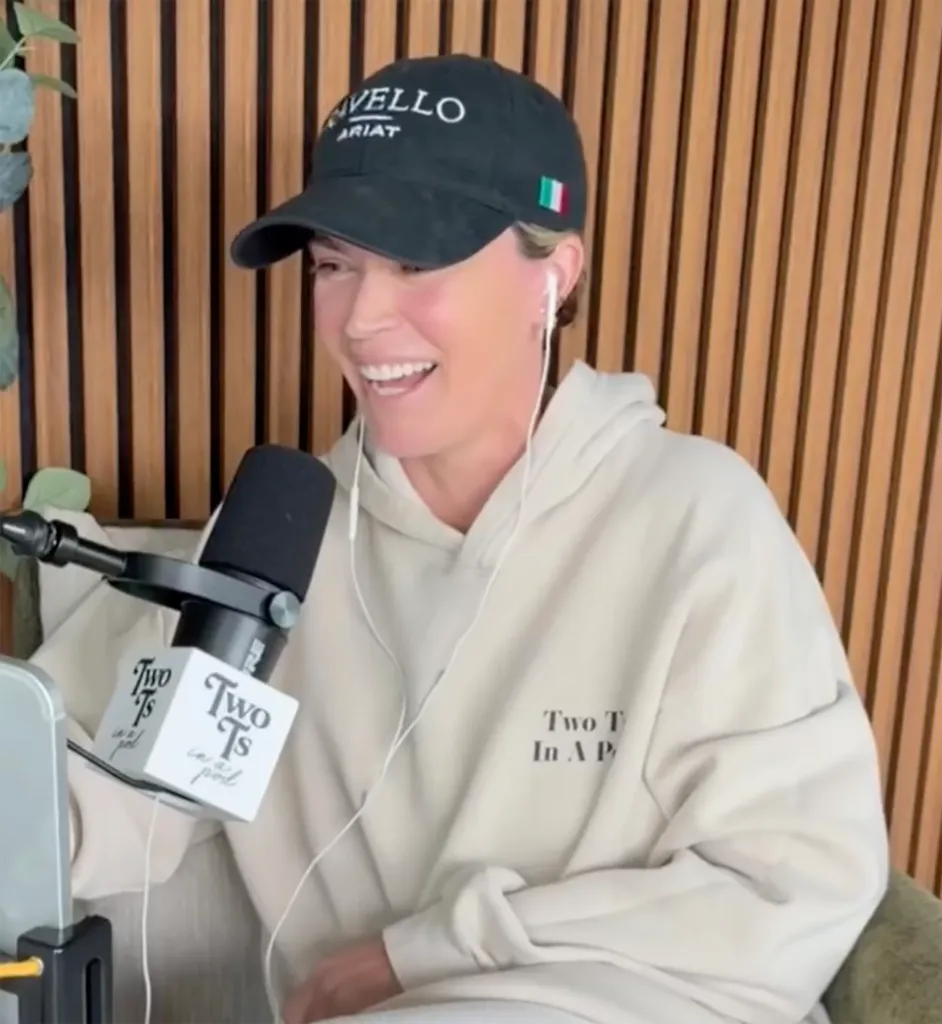 Teddi Mellencamp laughing while wearing a black baseball cap and a white hoodie, speaking into a microphone.