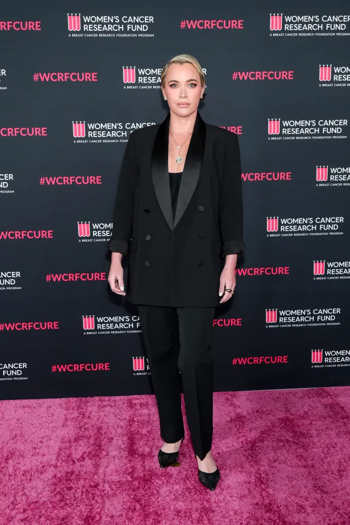 Teddi Mellencamp Arroyave in a black pantsuit, standing on a pink carpet in front of a Women's Cancer Research Fund backdrop.