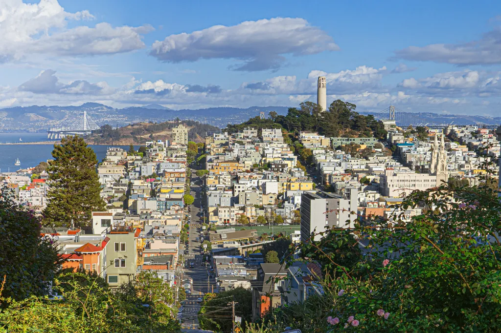 View of San Francisco from a high viewpoint, with Telegraph Hill, Lombard Street, Yerba Buena Island, The Bay Bridge, Treasure Island, Coit Tower, and the San Francisco Bay visible.