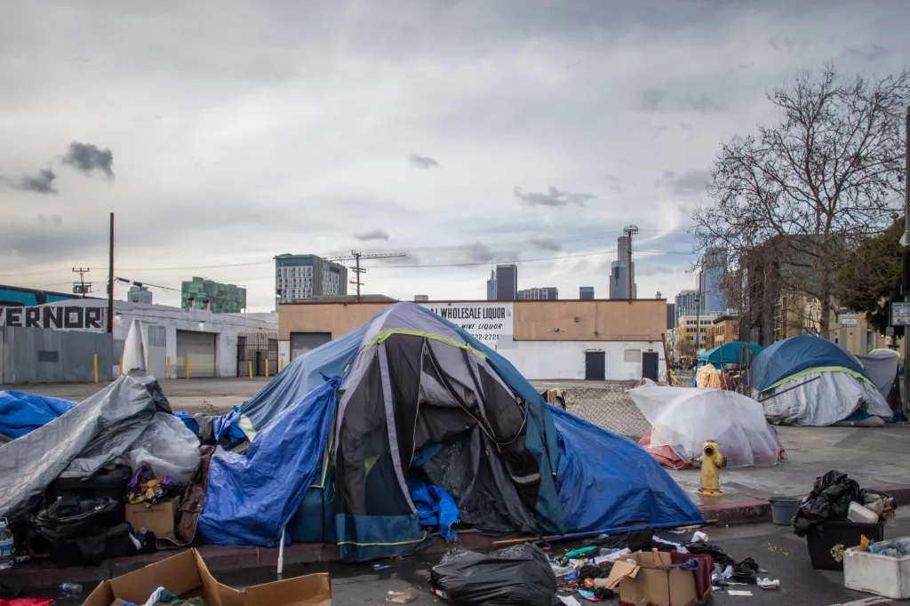 Tents and trash on the street in Skid Row, Los Angeles, with a city skyline in the background.