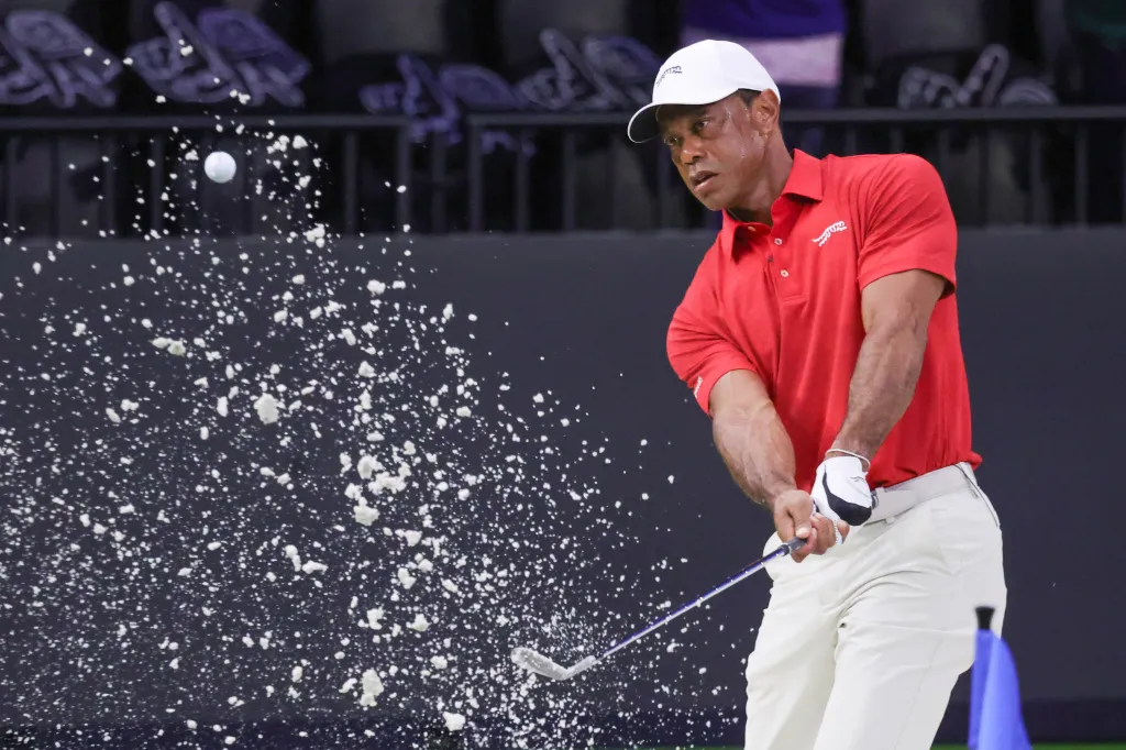 Tiger Woods hitting a golf ball out of a bunker, sending sand flying.