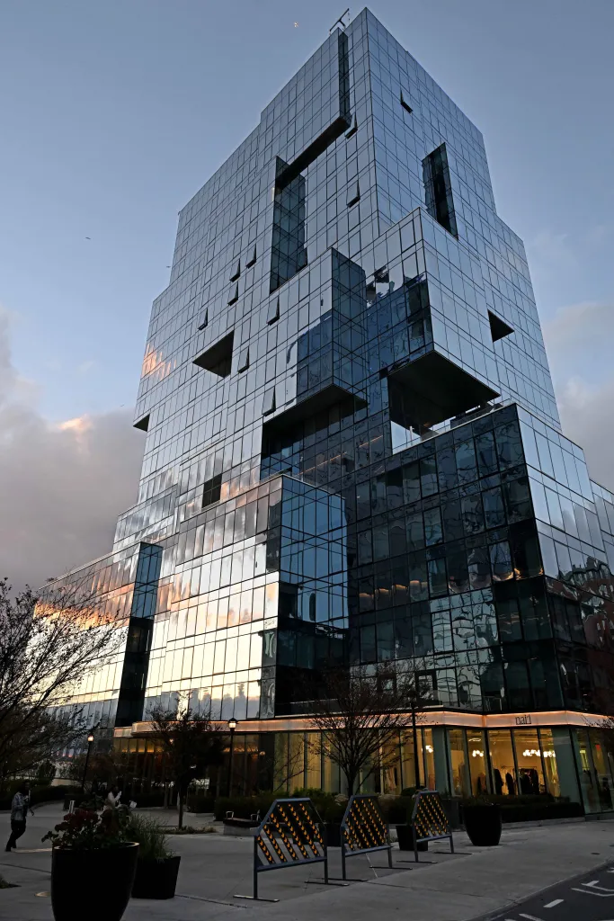 The glass facade of 416 Kent Avenue reflects the sky and sunset colors.