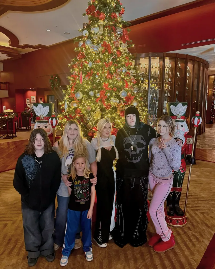 A large family, with a man and a woman surrounded by six children of varying ages, standing in front of a decorated Christmas tree.