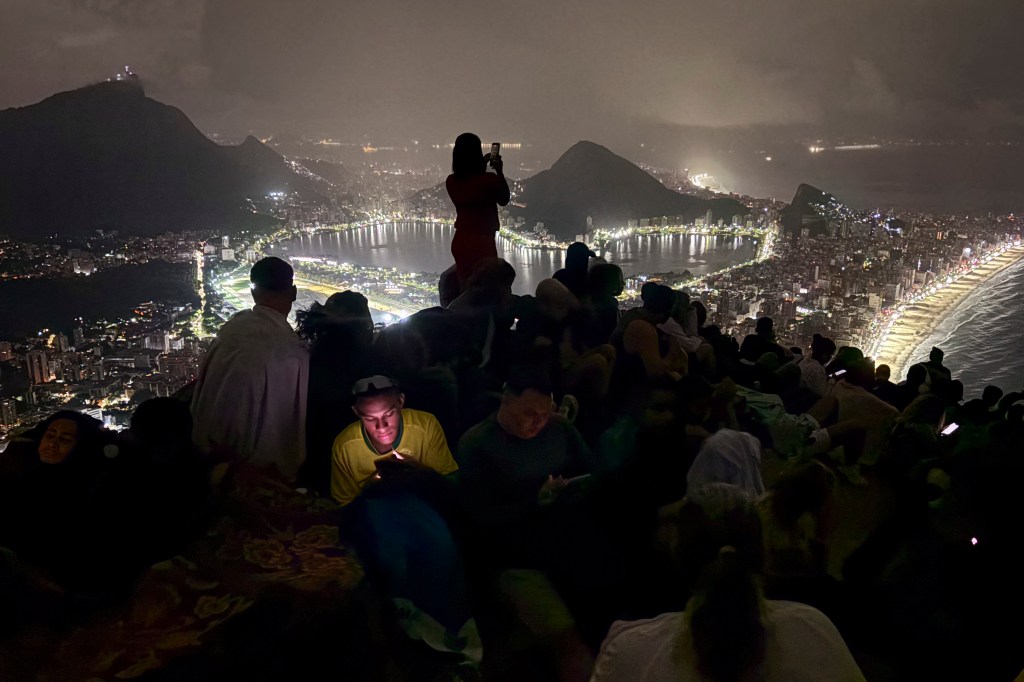 Tourists watch the sunrise from Morro Dois Irmaos overlooking the illuminated city and beach of Rio de Janeiro.