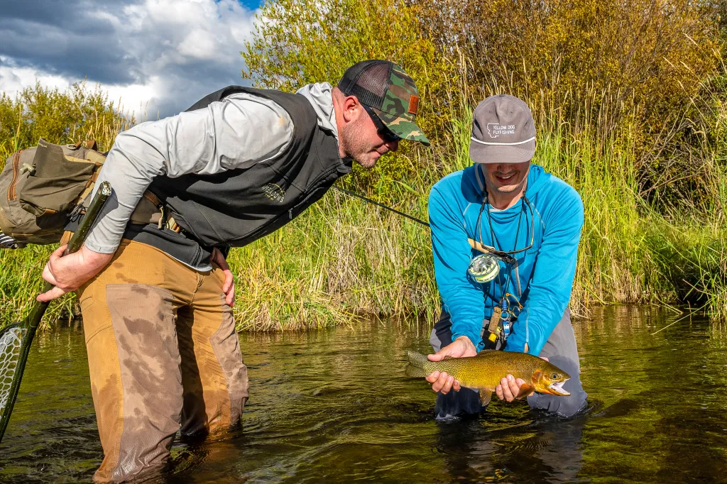 Two men fly-fishing in Rock Creek, Montana, holding up a golden-colored fish.