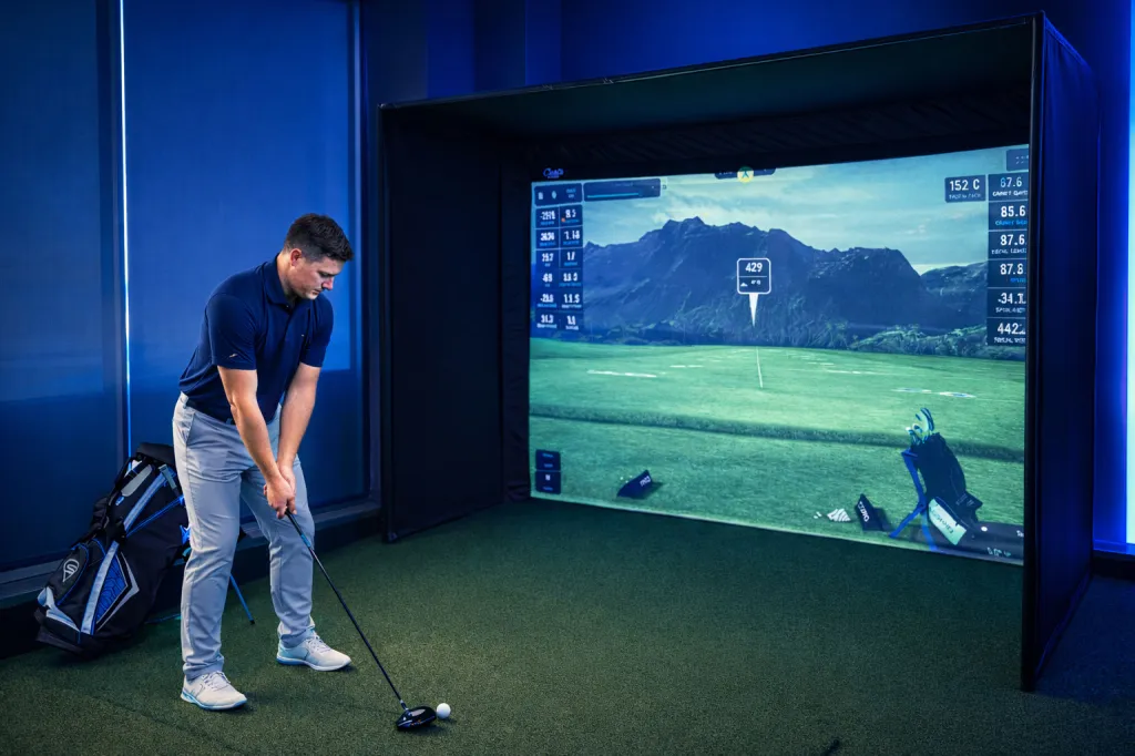 A man plays golf on a virtual simulator that projects a golf course onto a screen.