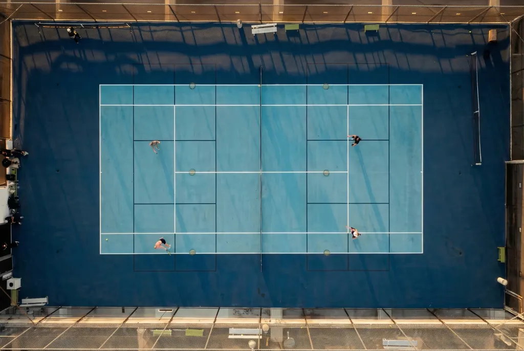 Aerial view of a tennis and pickleball court on a hotel roof with four people playing.