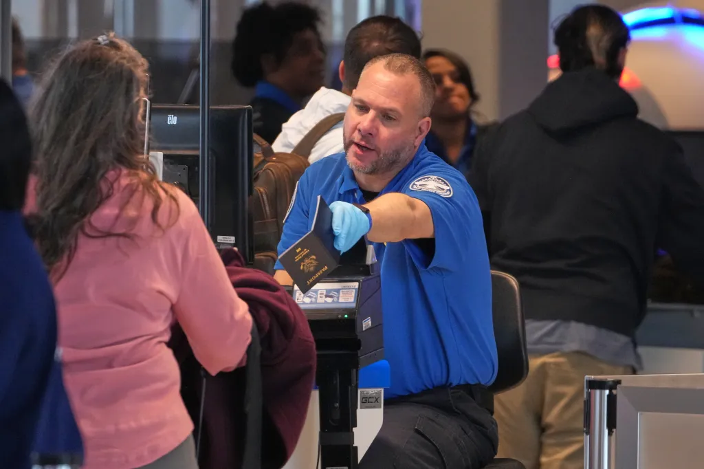 A TSA agent hands a passport back to a passenger at an airport security checkpoint.