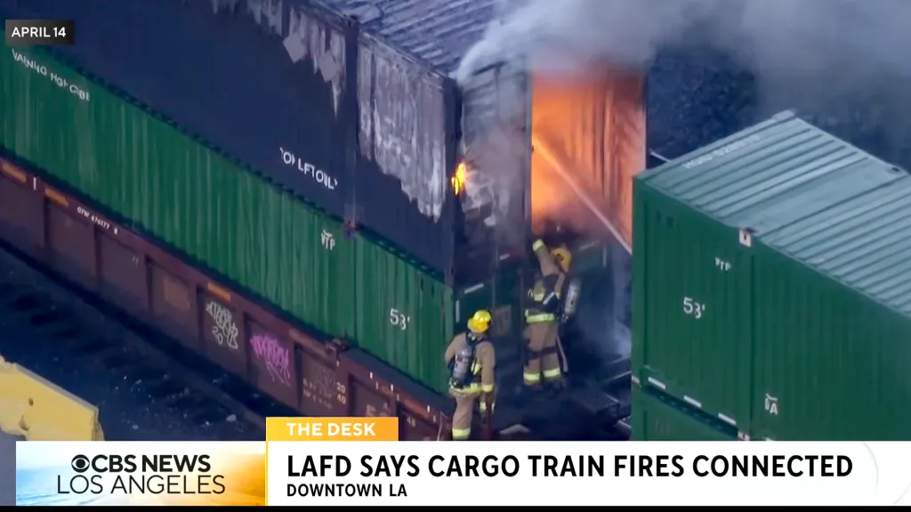 Two firefighters battling a fire engulfing a cargo train container.