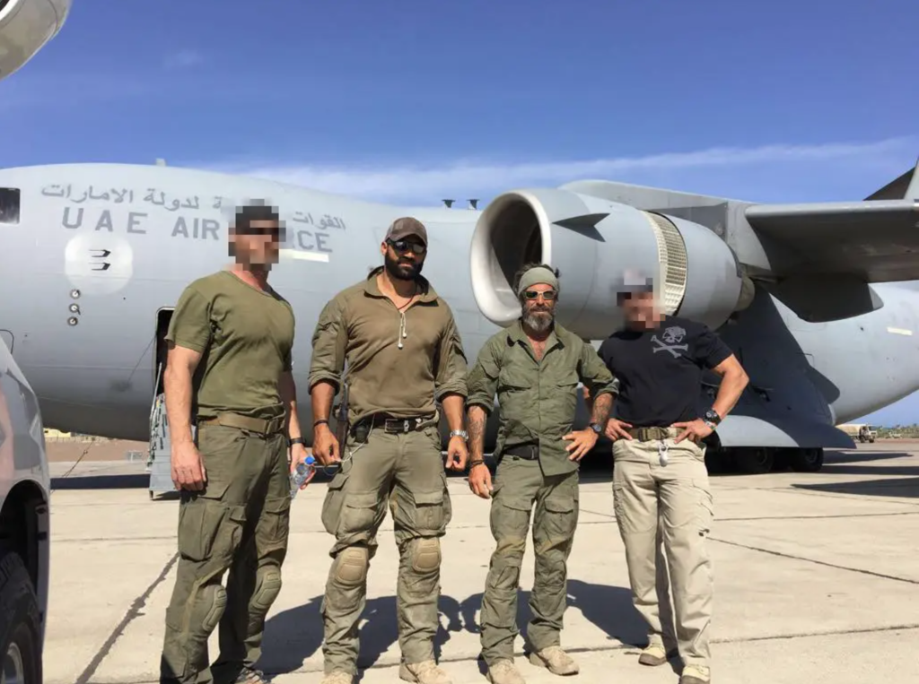 Gilmore, Golan, and two other mercenary team members stand in front of a UAE military plane.