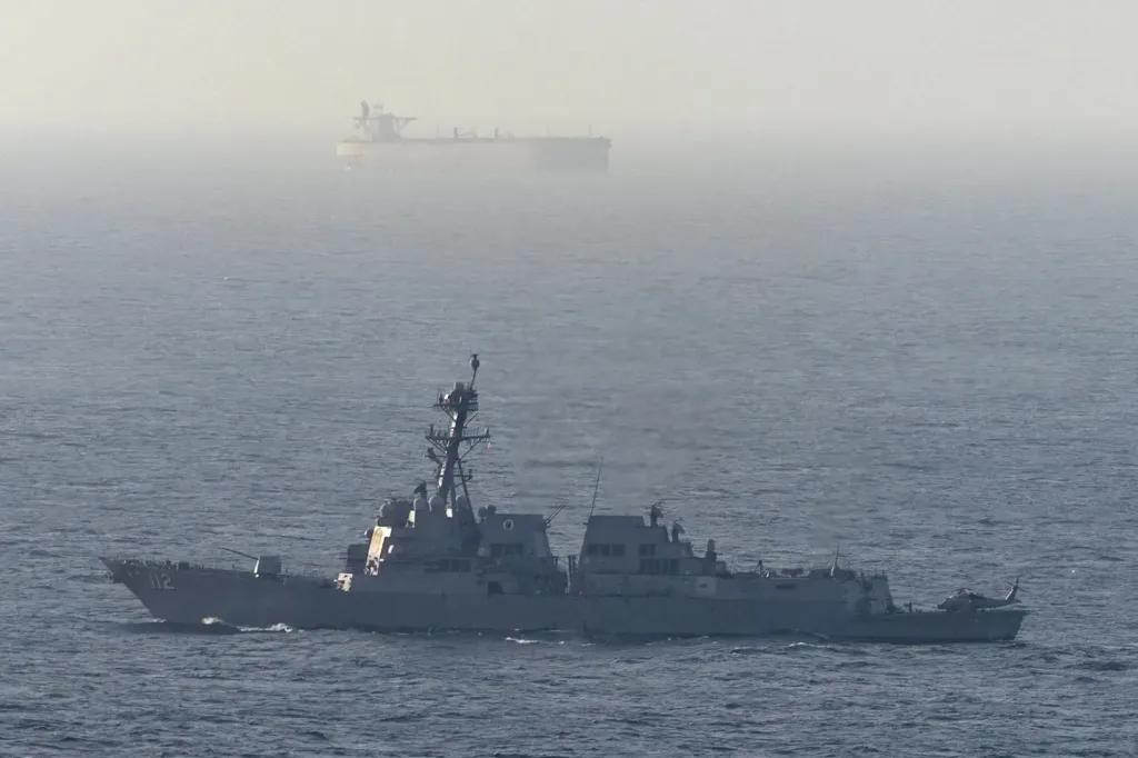 US Navy destroyer on patrol in the Gulf of Oman, with a cargo ship in the hazy background.