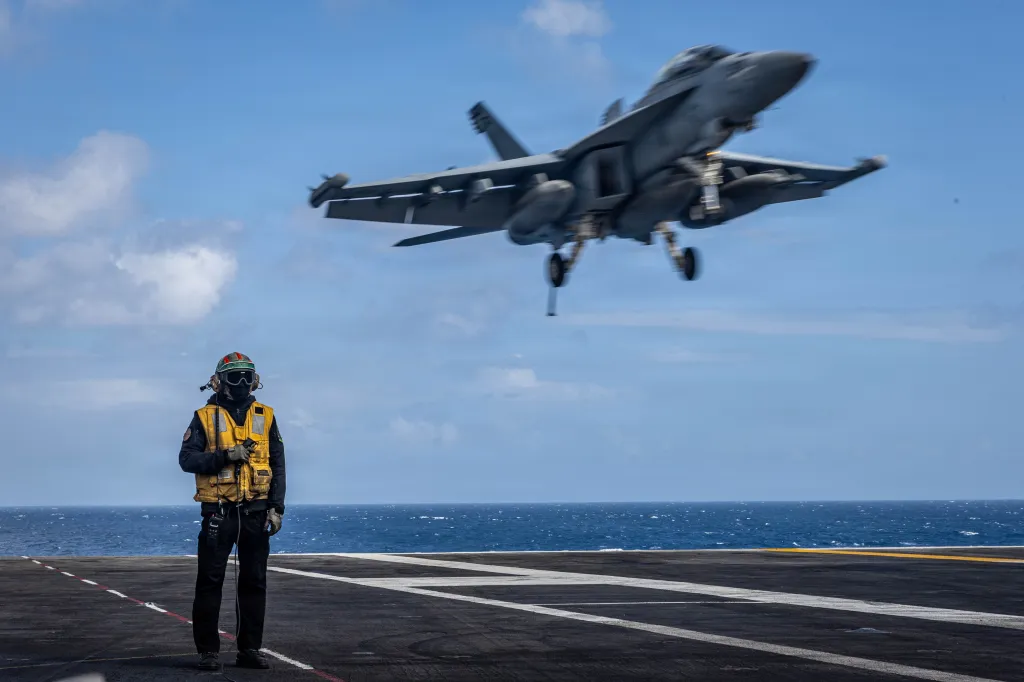 U.S. Navy Aviation Boatswain's Mate 3rd Class Bruce Brown on the flight deck of the USS Gerald R. Ford as an F/A-18E Super Hornet approaches for landing.