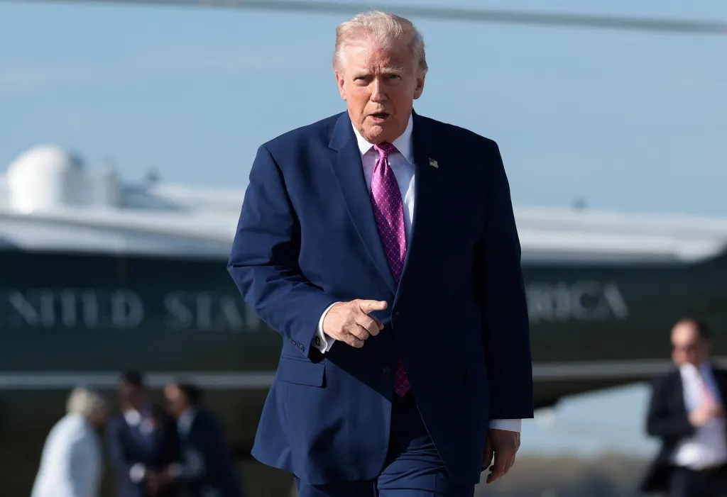U.S. President Donald Trump in a navy suit and pink tie gestures before boarding Air Force One.