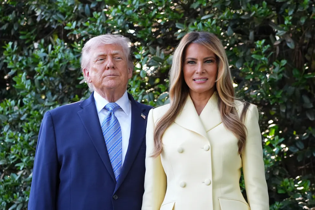 Former President Donald Trump and Melania Trump stand in front of greenery.