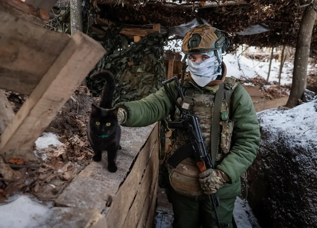 A Ukrainian serviceman pets a black cat in a trench