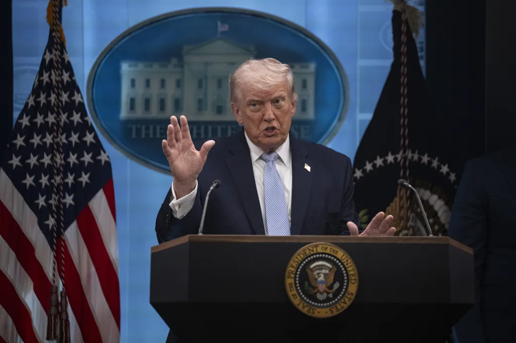 President Donald Trump speaking at a press conference, with the Presidential seal on the podium and US flags behind him.
