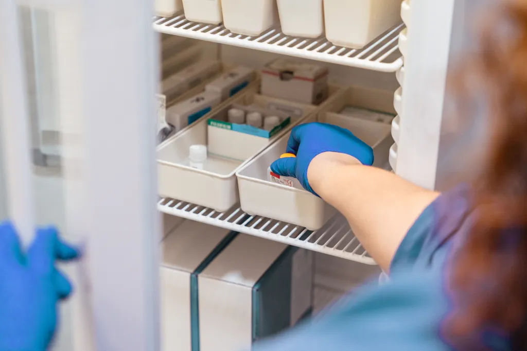 Nurse in blue gloves taking inventory of medical supplies from a hospital refrigerator.