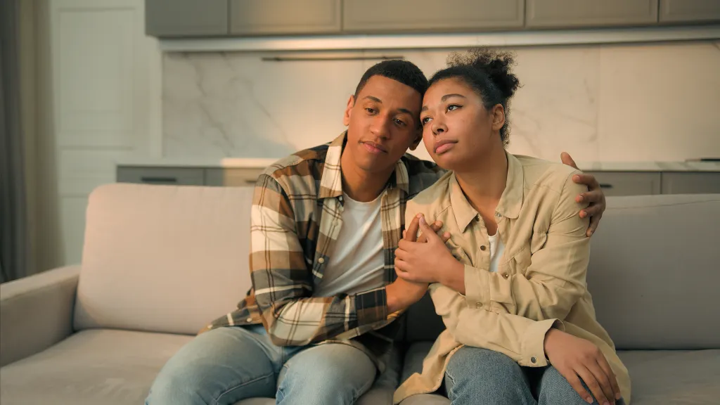 A sad African American couple embracing on a sofa, worried about moving out.