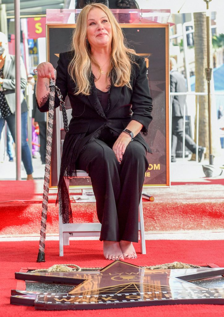 Christina Applegate sits barefoot on a white chair, holding a walking stick, on the Hollywood Walk of Fame.