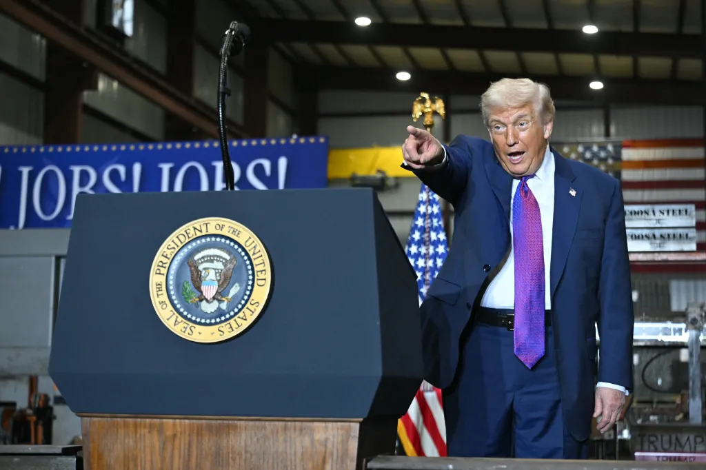 Donald Trump points to the audience while speaking at a podium with the Seal of the President.