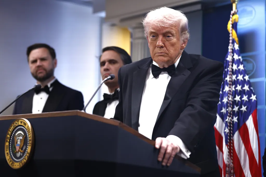 Donald Trump in a tuxedo speaking from a podium with the Seal of the President of the United States.