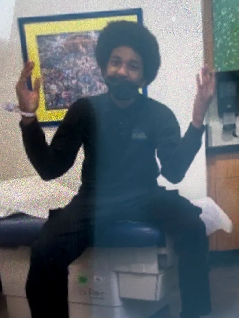 Najeir Allen with an afro and black clothing, making a peace sign with both hands.