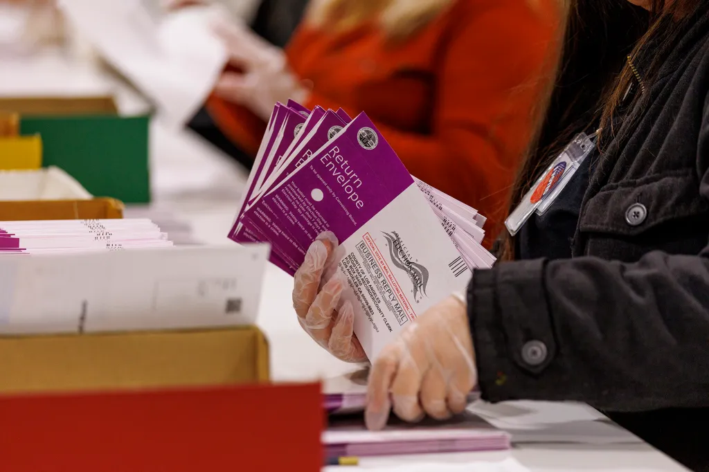 A person wearing gloves inspects vote-by-mail ballots at the Los Angeles County Ballot Processing Center.
