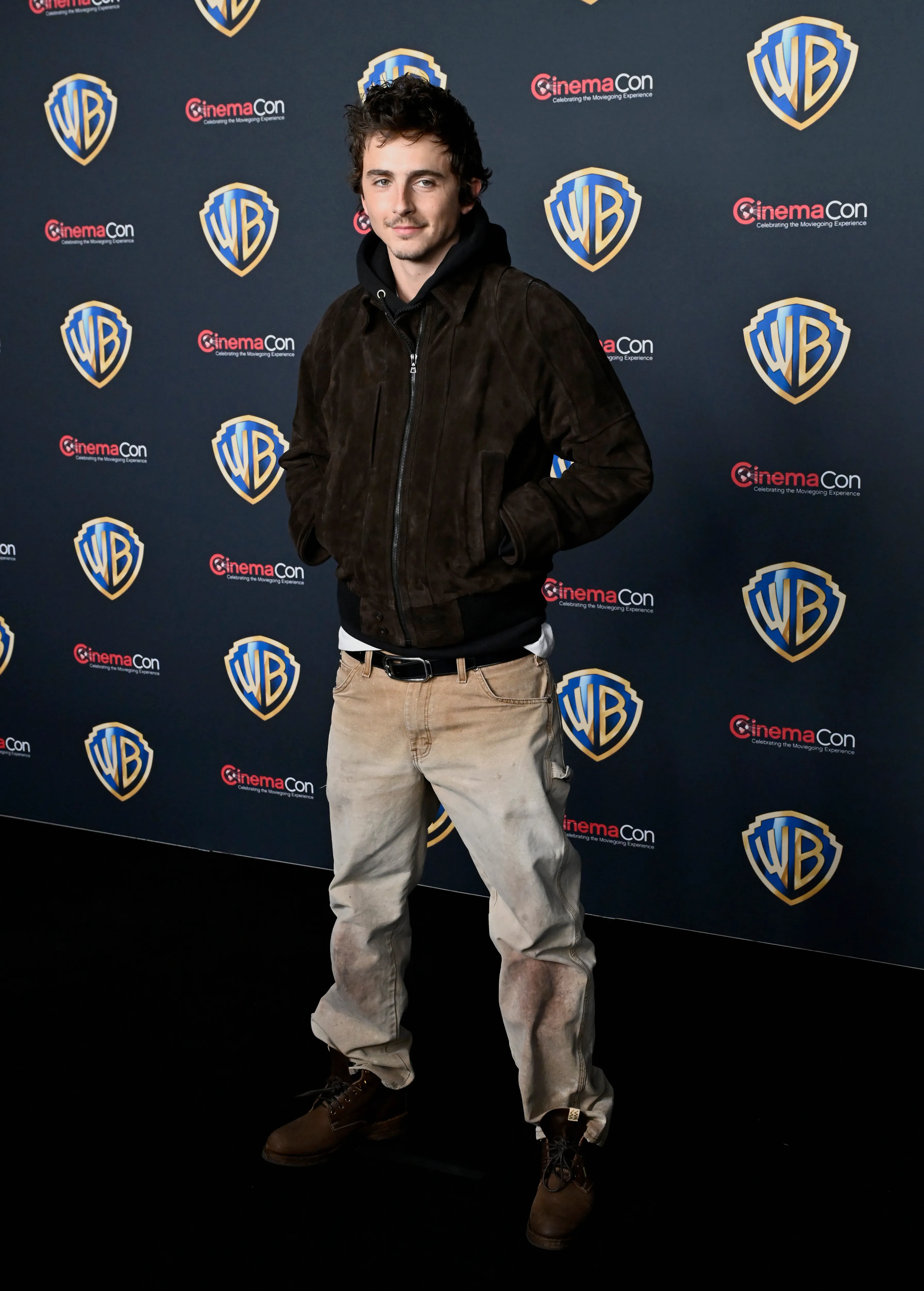 Timothée Chalamet standing on a red carpet in front of a backdrop with Warner Bros. and CinemaCon logos.