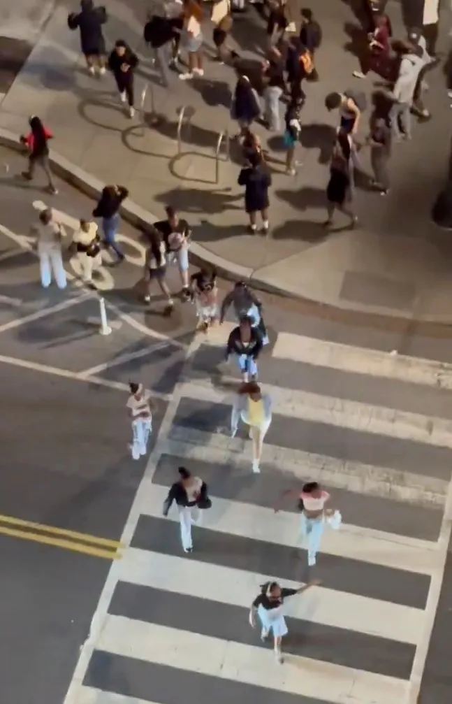 An aerial shot of a large group of young people gathered on a street corner and in a crosswalk.