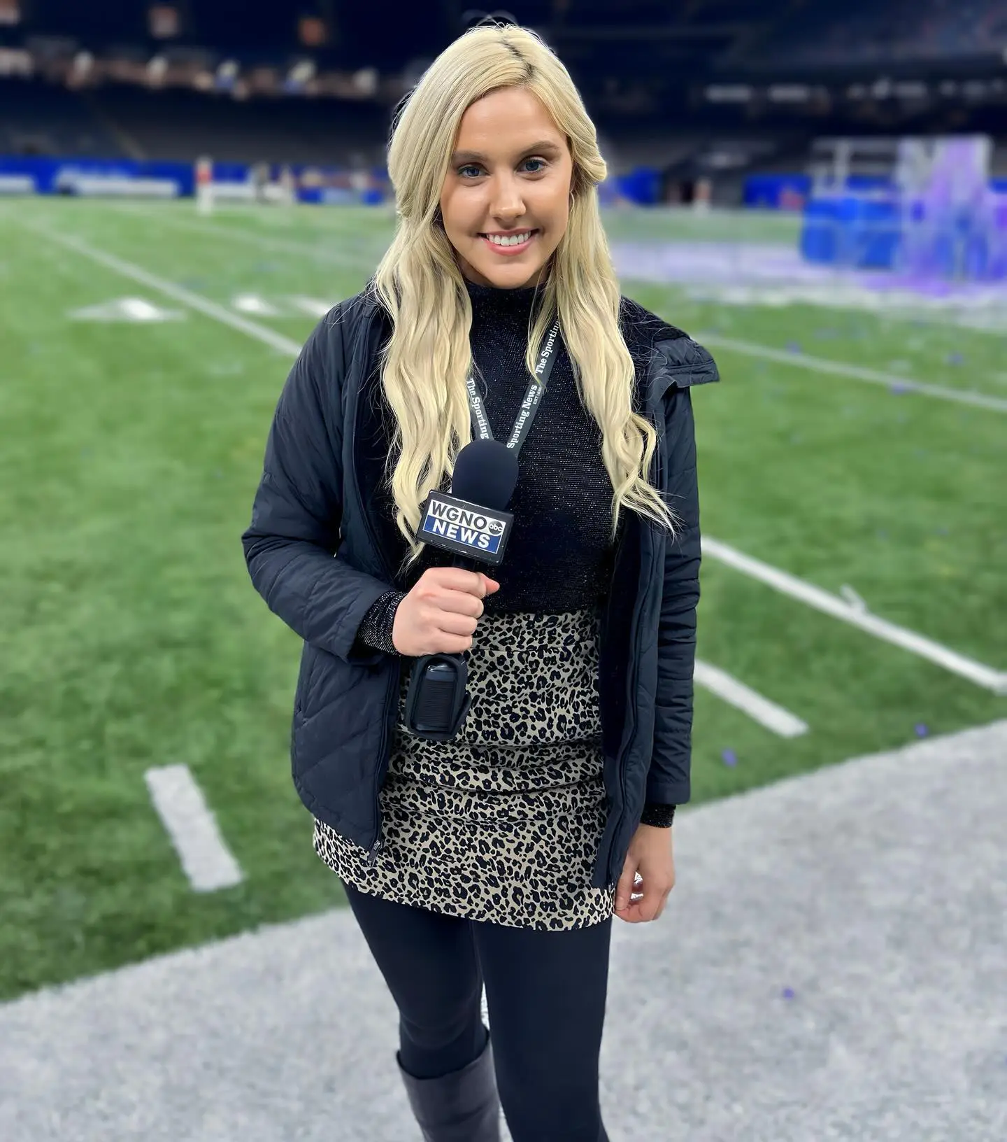 Crissy Froyd woman reporter in a black jacket and leopard print shirt holding a WGNO News microphone on a football field.