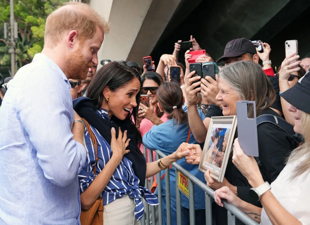 Meghan Markle and Prince Harry interacting with well-wishers, one of whom is presenting a framed photograph.