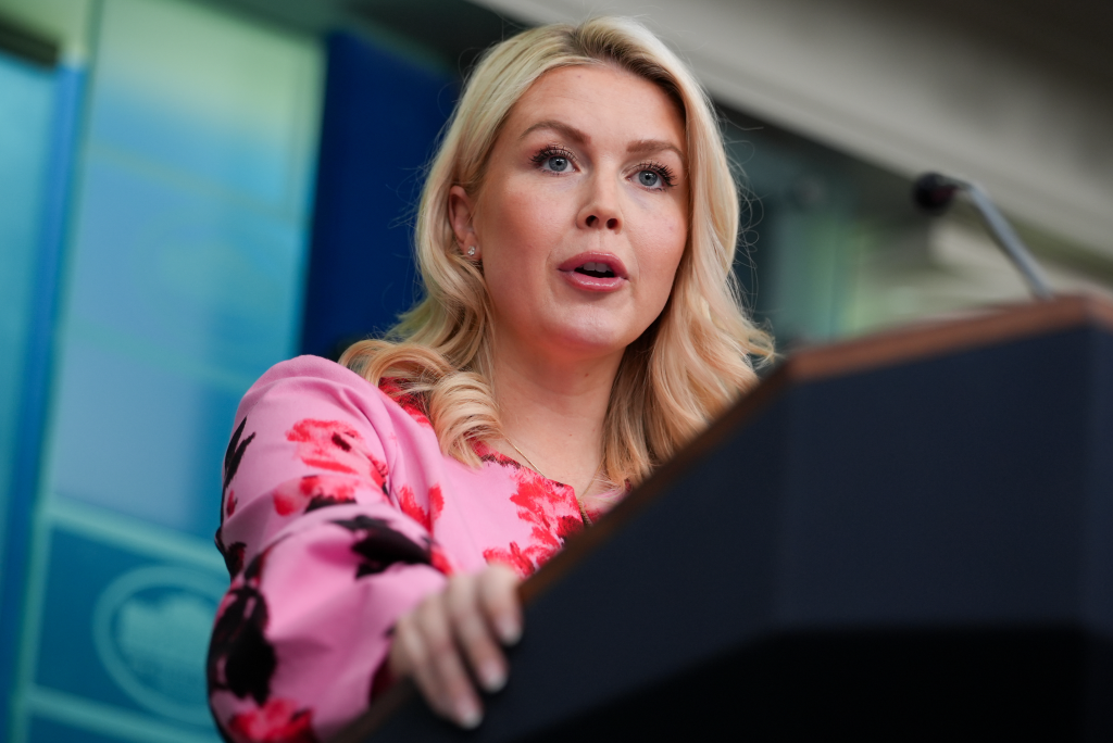 President Biden speaking at a podium with Press Secretary Karine Jean-Pierre in the background.