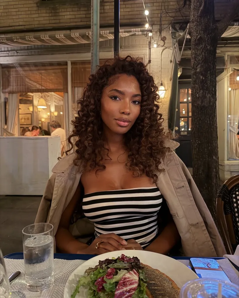 Tatiana Elizabeth at a restaurant with a trench coat draped over a striped top.