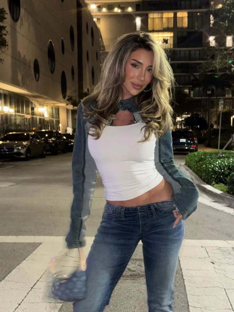 Influencer Lauren Blake Boultier in a white top, denim jacket, and jeans posing at night.