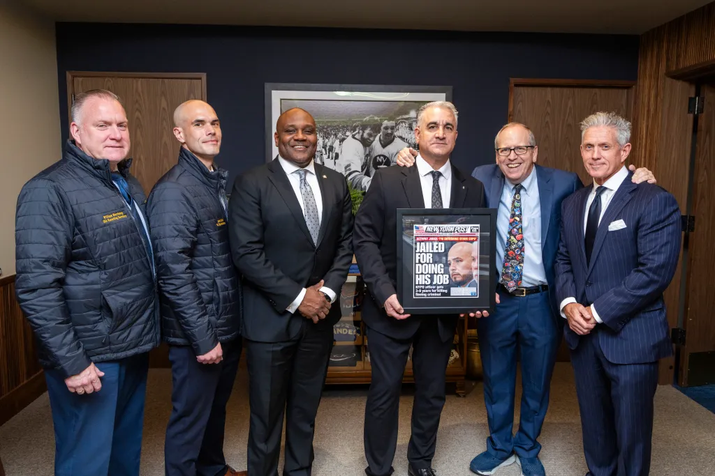 Six men gather, one holding a framed newspaper front page with the headline