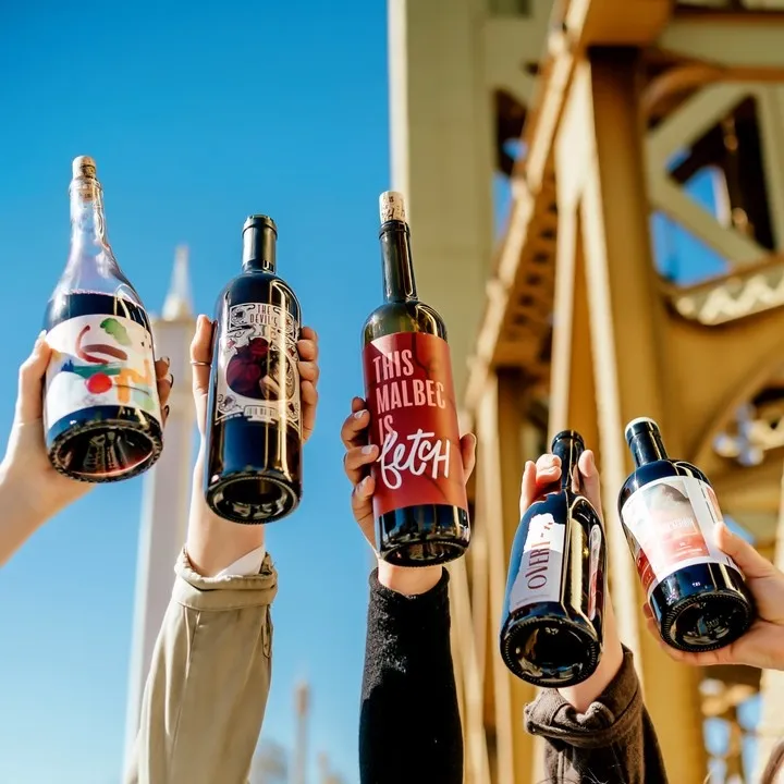 People holding up five bottles of eStCru wine against a blue sky and bridge structure.