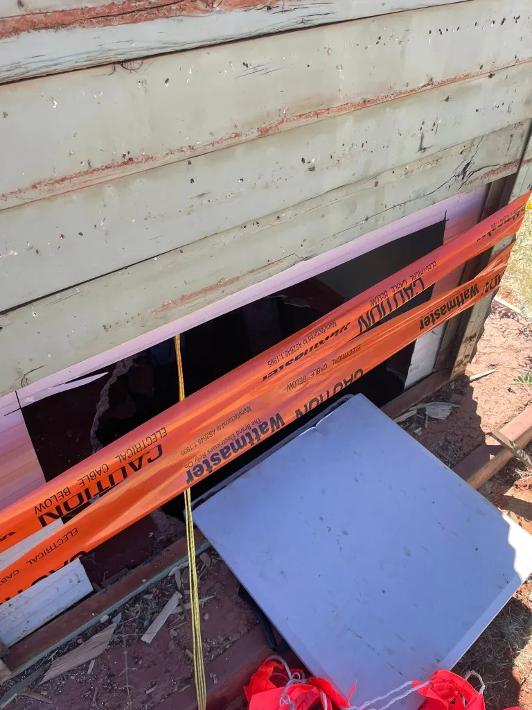 A roadside drop toilet with caution tape across a deep pit.