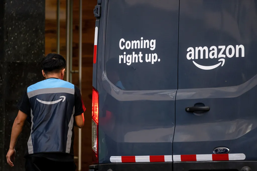 An Amazon delivery worker in uniform walks past an Amazon delivery vehicle.