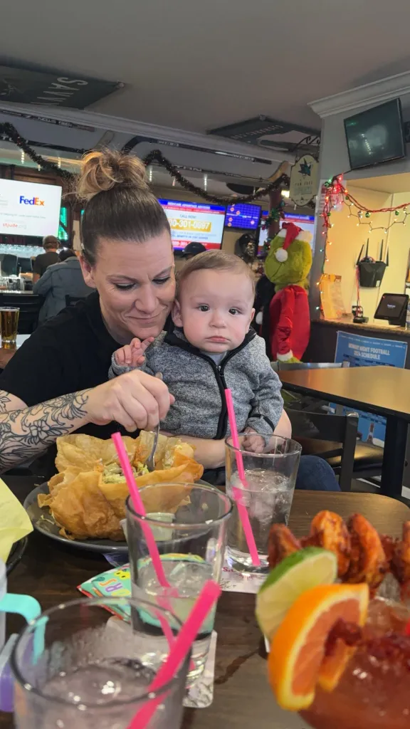 A woman holds baby Jaxon while eating a taco salad at a restaurant.