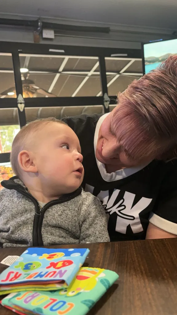 Baby Jaxon looks up at an adult with pink hair.