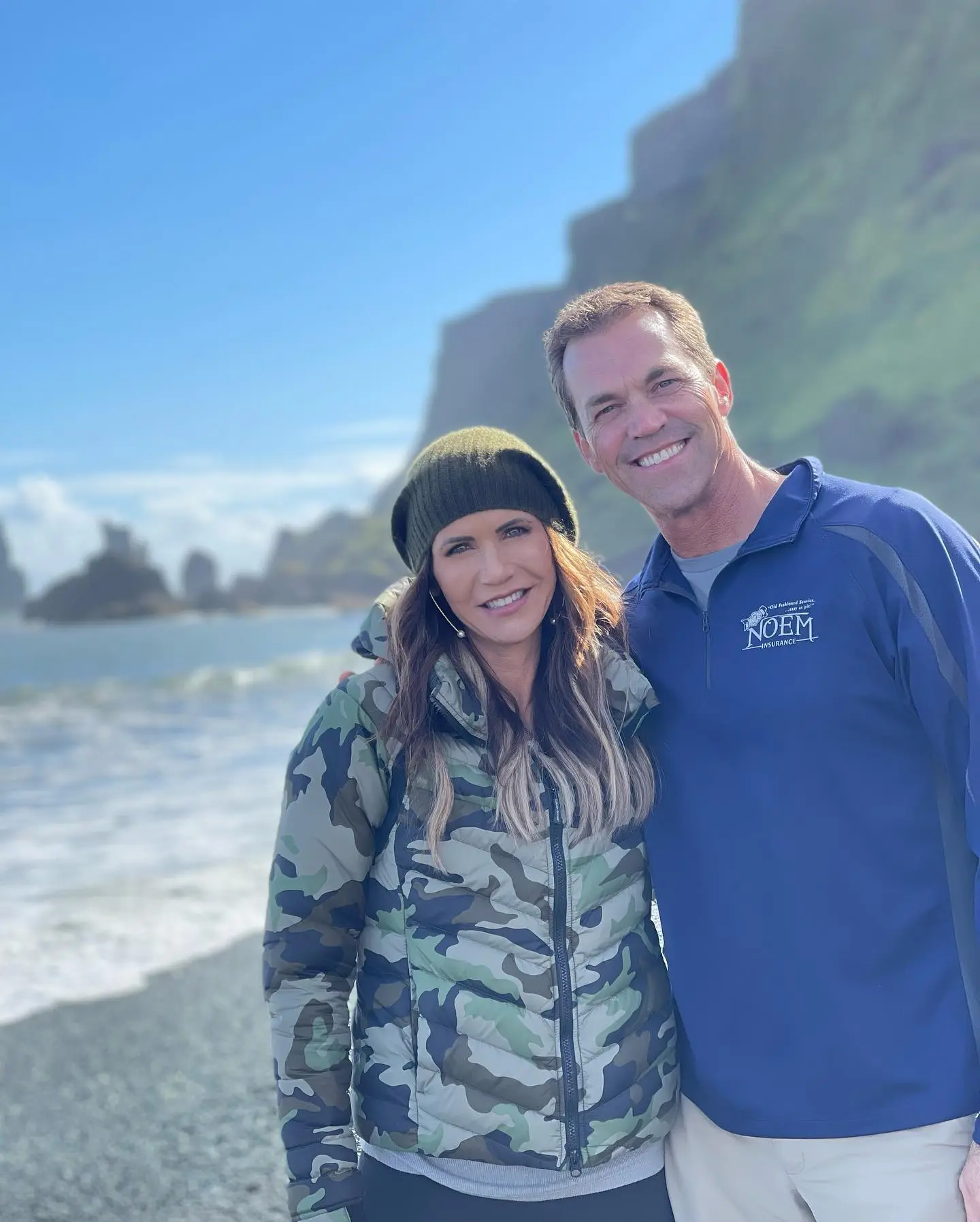 Kristi and Bryon Noem standing on a rocky beach with cliffs and sea stacks in the background.