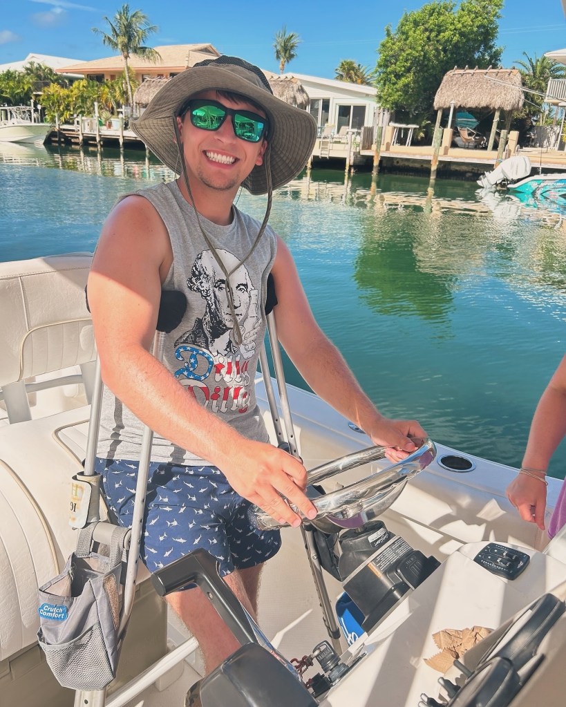 Dylan Carter steering a boat with crutches.