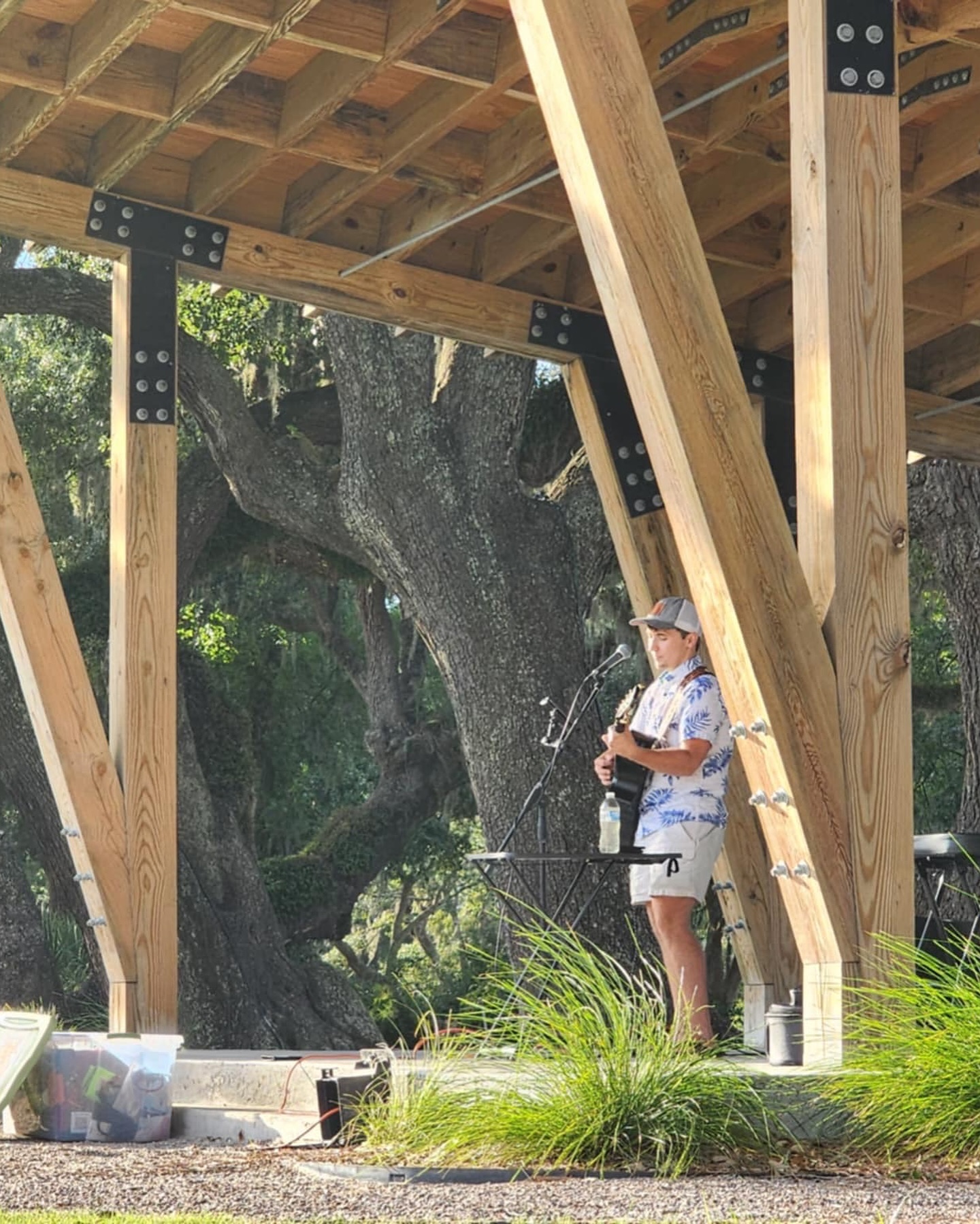 Dylan Carter performing outside on a flatbed trailer stage, playing an acoustic guitar and singing into a microphone.