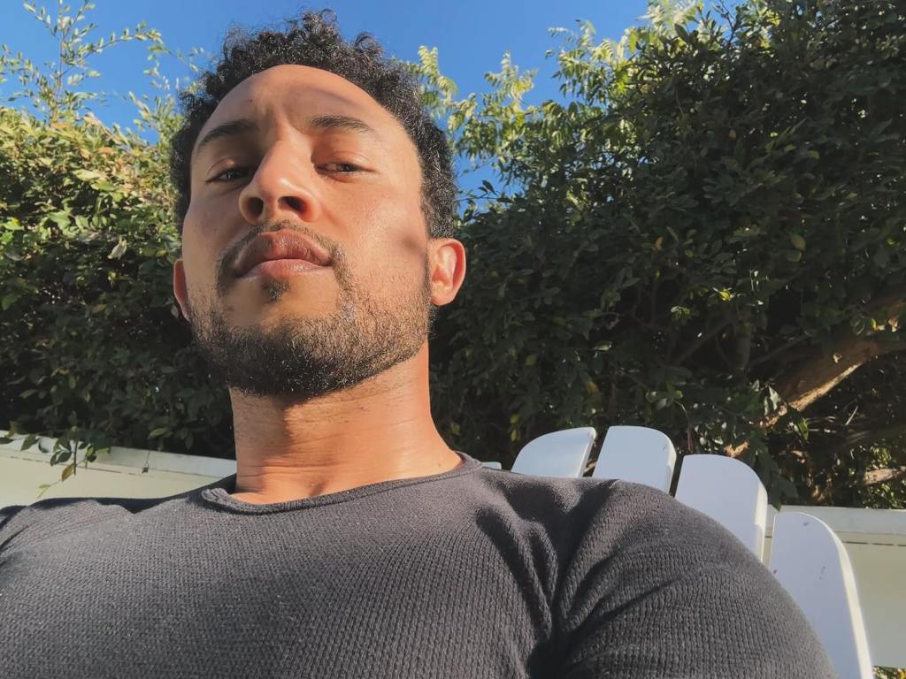 Tahj Mowry taking a selfie outdoors, sitting in a white Adirondack chair.
